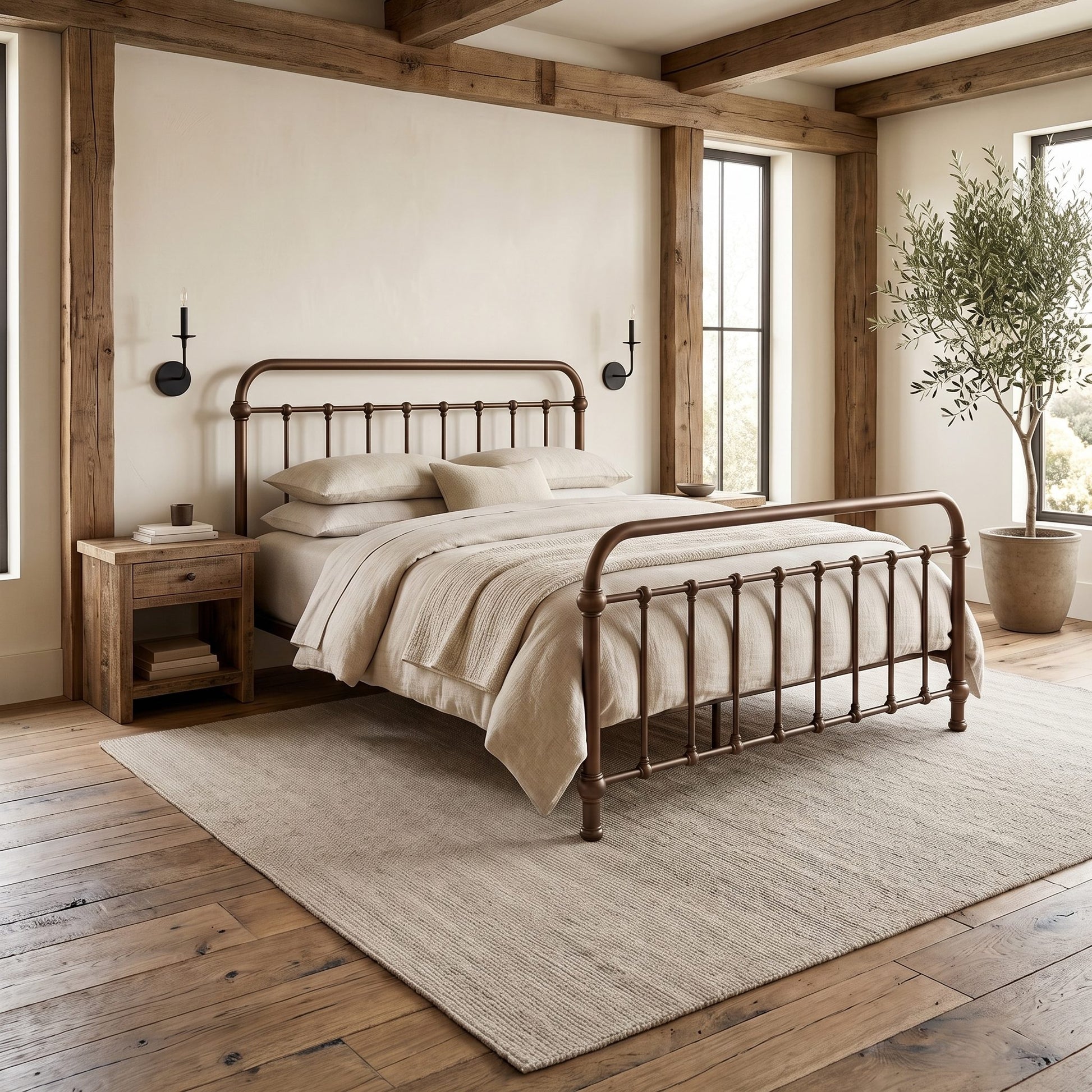 Heiressy 20th c Americana Iron Bed in Copper Wash finish with a curved headboard and footboard, styled in a warm, neutral-toned bedroom with a matching nightstand, textured rug, and wooden ceiling beams.