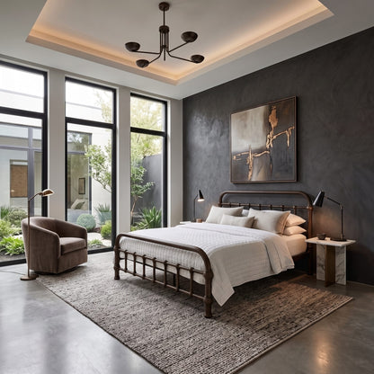 20th c Americana Low Profile Iron Platform Bed by Heiressy. A modern bedroom interior featuring a dark wood bed frame with white bedding, set on a textured area rug against a dark gray wall with a large abstract painting. The room includes a brown armchair, a black multi-arm ceiling light, and large windows looking out to a garden.