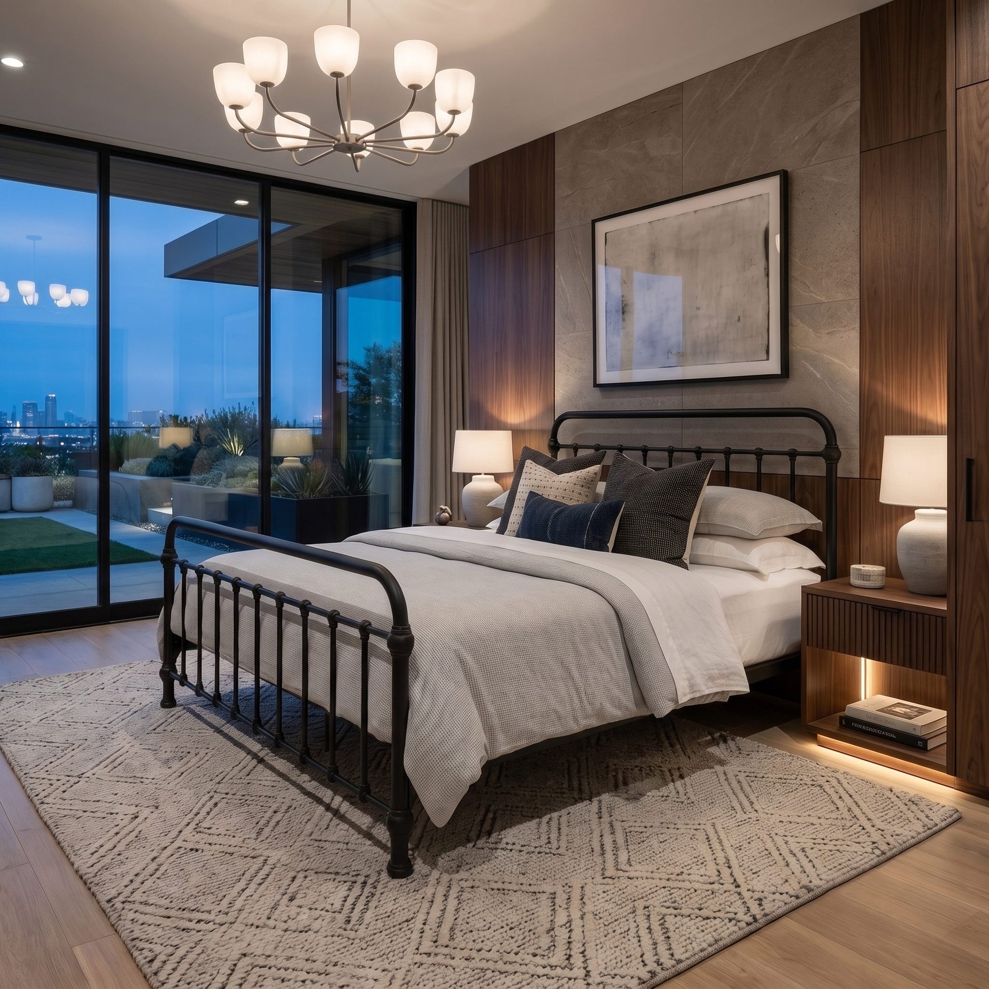 Heiressy 20th c Americana Iron Bed in Matte Black Finish. A modern bedroom featuring a black metal bed frame with white bedding, styled with dark accent pillows, set on a patterned rug against a wood-paneled wall with a chandelier and large windows overlooking a city skyline at dusk.