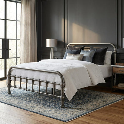 20th c Americana Low Profile Iron Platform Bed by Heiressy. A metal bed frame with turned legs and curved headboard/footboard, styled with white bedding and dark accent pillows in a dark paneled bedroom with a blue patterned rug.