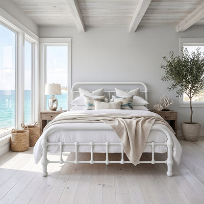 20th c Americana Low Profile Iron Platform Bed by Heiressy.  A white metal bed frame with a classic turned spindle foot design, styled with white linens, beige pillows, and a beige throw blanket in a bright, modern beach-style bedroom.